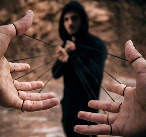 A hooded figure pulls black strings tied to a person's hands, symbolising manipulation in social engineering attacks