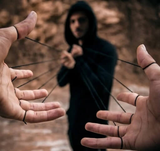 A hooded figure pulls black strings tied to a person's hands, symbolising manipulation in social engineering attacks